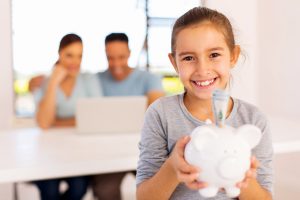 cheerful little girl holding piggybank with parents on background