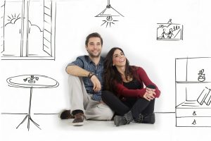 Young couple sitting on floor looking up while dreaming their new home and furnishing.